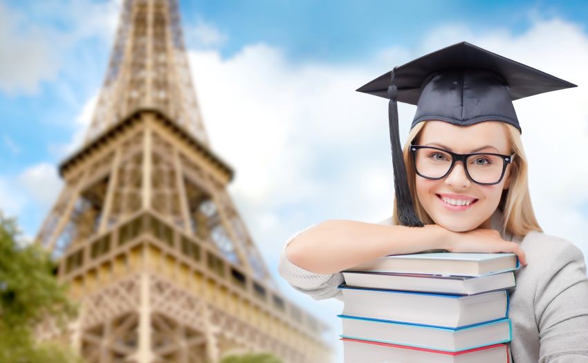 Étudiante en mathématiques diplômée souriante avec une pile de livres devant la Tour Eiffel à Paris
