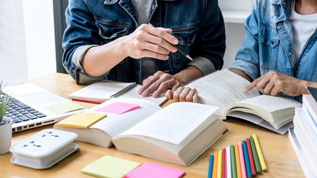 Un professeur aide un élève à réviser avec des manuels ouverts et un ordinateur portable