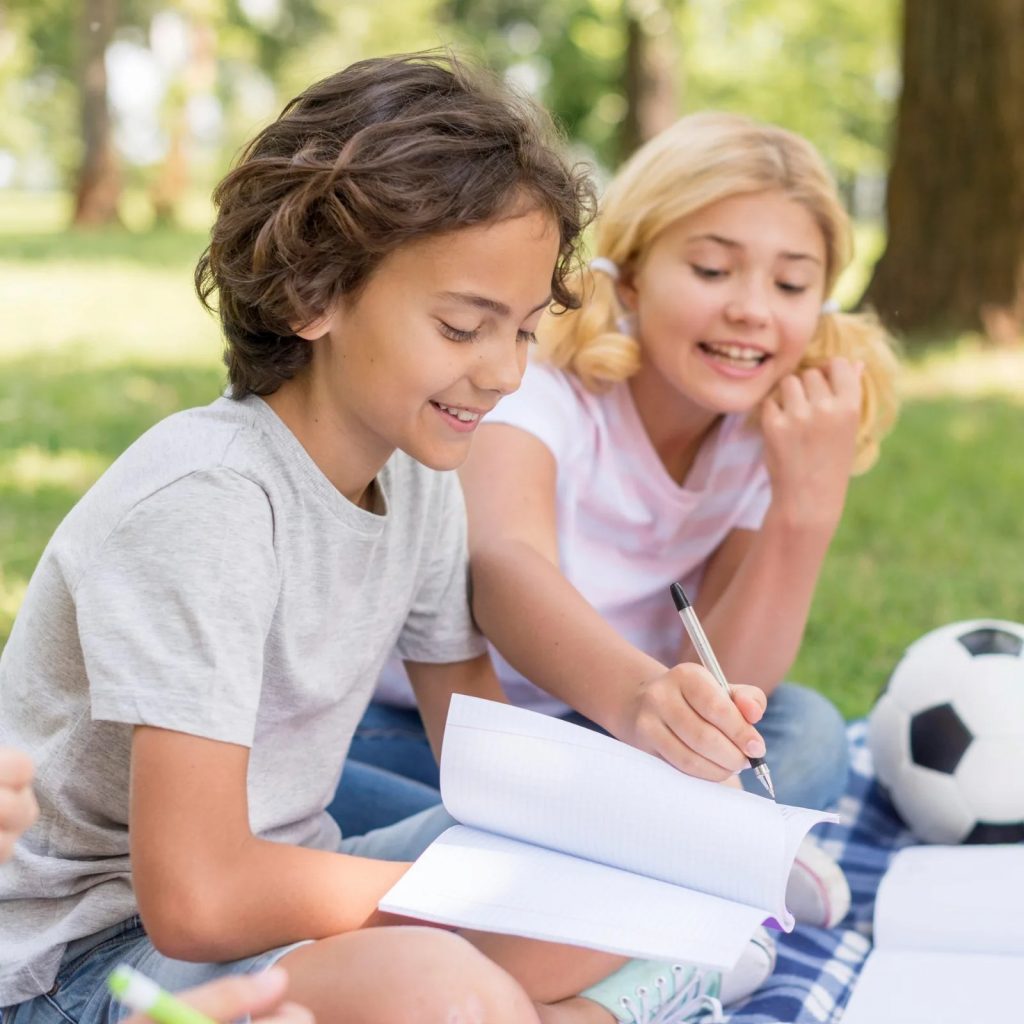 Deux enfants révisent ensemble dans un parc pendant les vacances d’été.